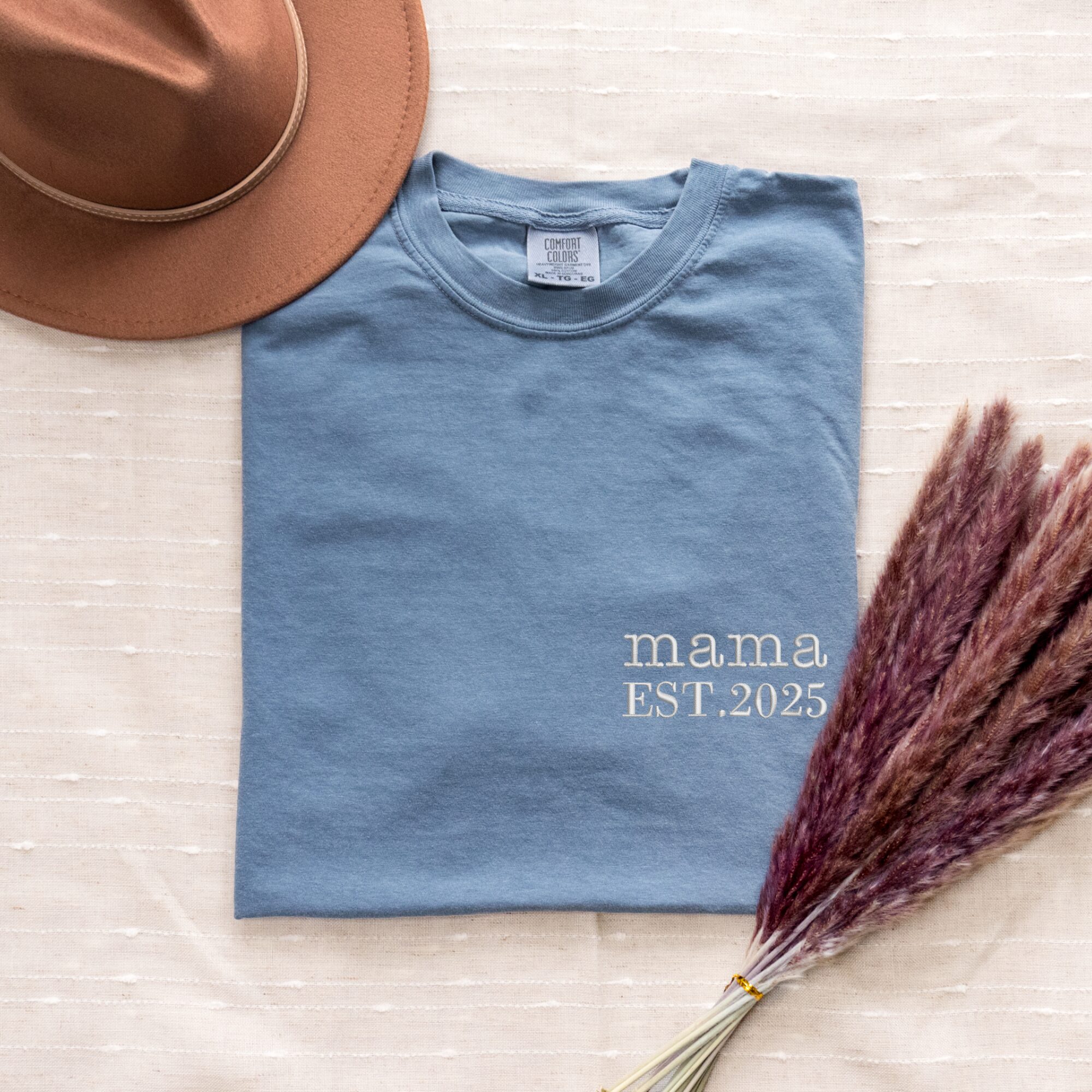 Blue Jean Comfort Colors Mama T-Shirt worn oversized by woman, white 'mama EST. 2025', casual styling.